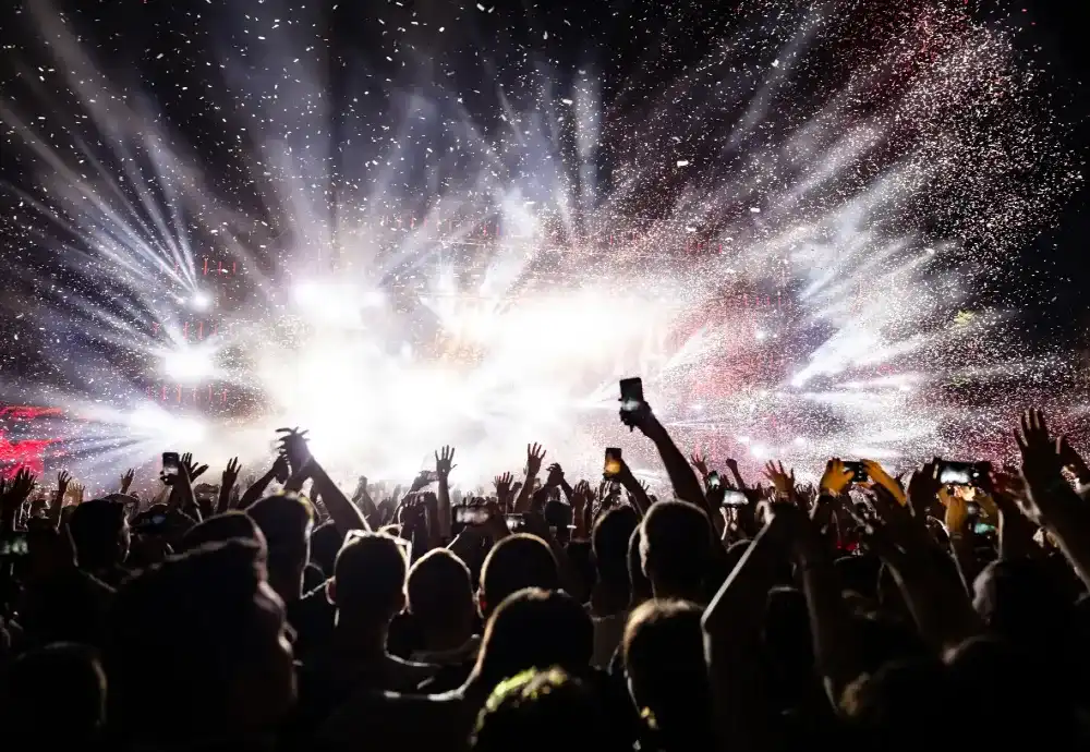 Excited concert crowd under bright stage lights and confetti at a live music event in Hong Kong.