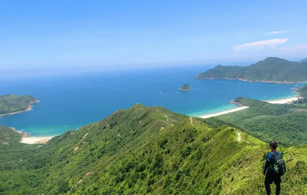 Hiker overlooking lush green hills and bays along the Lantau Peak Hong Kong Hiker overlooking lush green hills and bays along the Lantau Peak Hong Kong